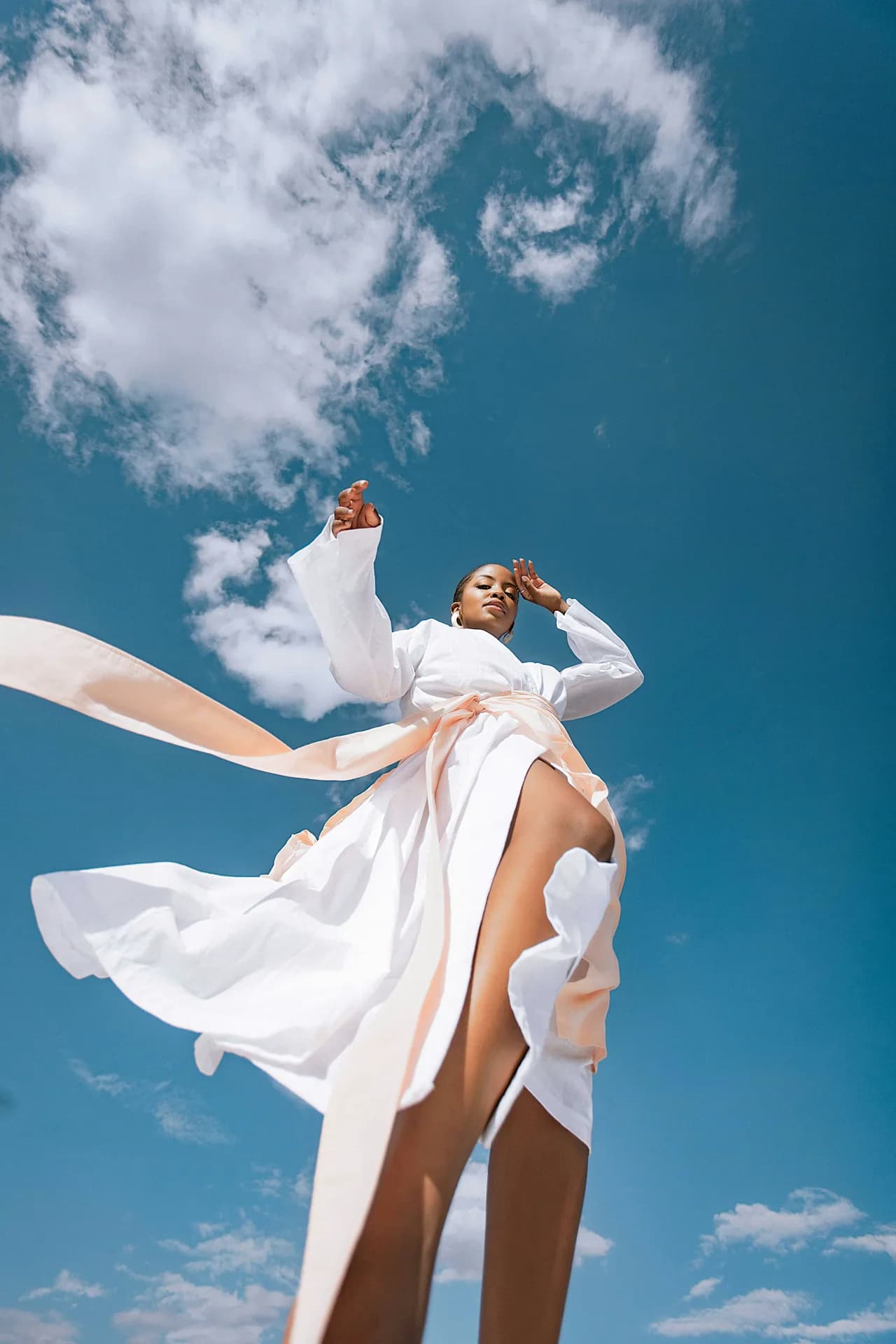 A fashion portrait with a white dress against a blue sky.